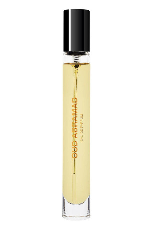 A cylindrical perfume bottle with a black cap, containing yellow liquid, labeled "Oud Abramad" by BDK Parfums, evokes the essence of a desert night with its rich notes of Turkish Rose and Agarwood.