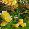 A bottle of perfume labeled "Zoologist Dodo Jackfruit Edition" rests on a green leaf surrounded by yellow jackfruit segments and white flowers, evoking the fragrance notes of an island forest, with a large halved jackfruit in the background.