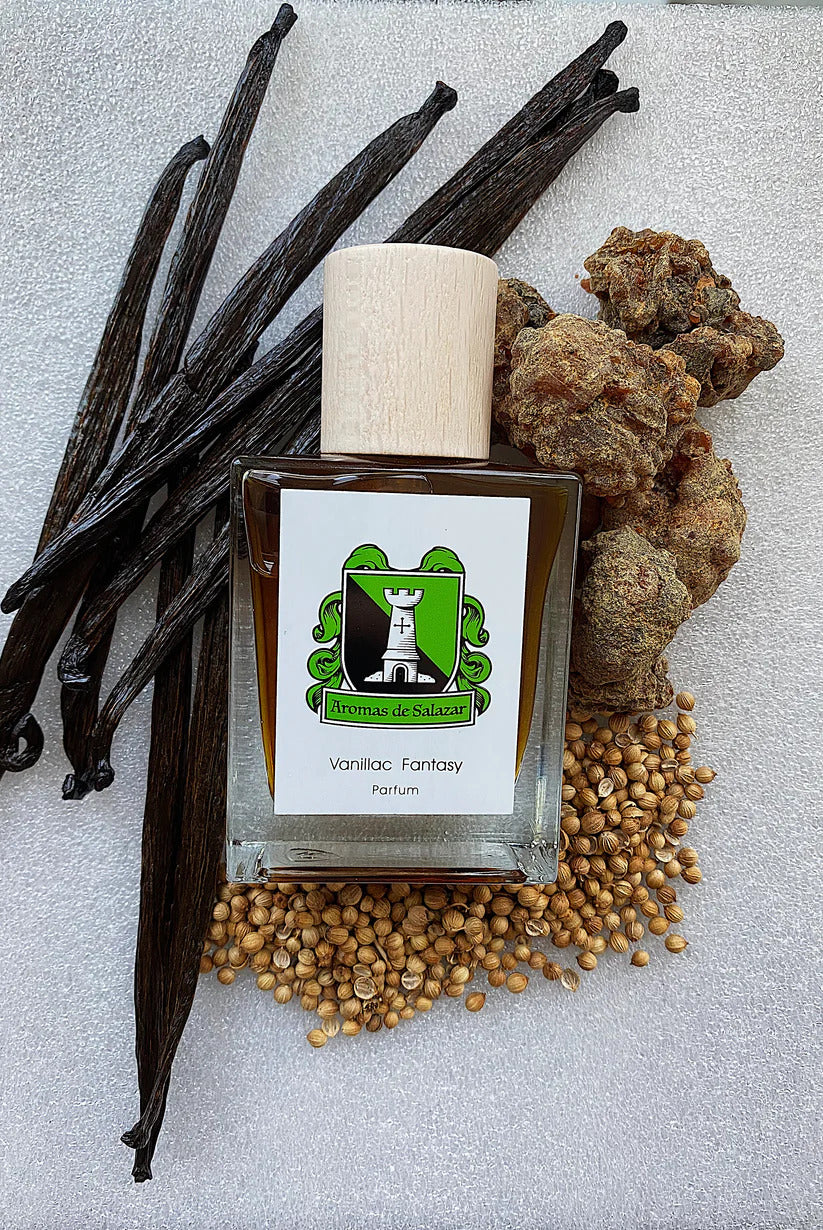 Bottle of Vanillac Fantasy by Aromas de Salazar, a unisex vanilla fragrance, is displayed with vanilla pods, seeds, and rocks on a textured white background.