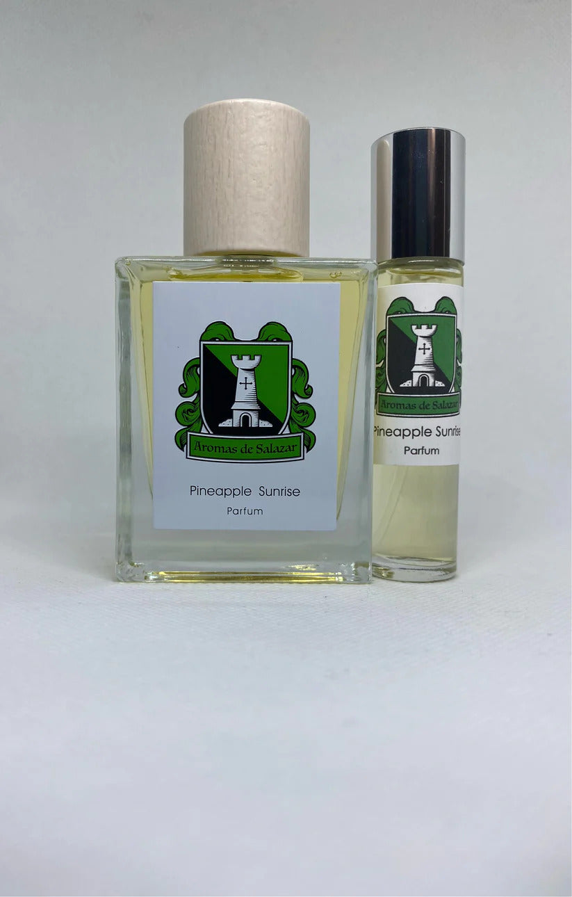 A bottle and a spray vial of "Pineapple Sunrise" by Aromas de Salazar, showcasing its seductive pineapple fragrance, are placed side by side against a plain background.