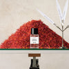 A small bottle labeled "CRYSTAL SAFFRON" by Matiere Premiere is placed in front of a pyramid-shaped pile of saffron strands, with white scent strips standing in a holder nearby, subtly hinting at the delicate notes of saffron oil.