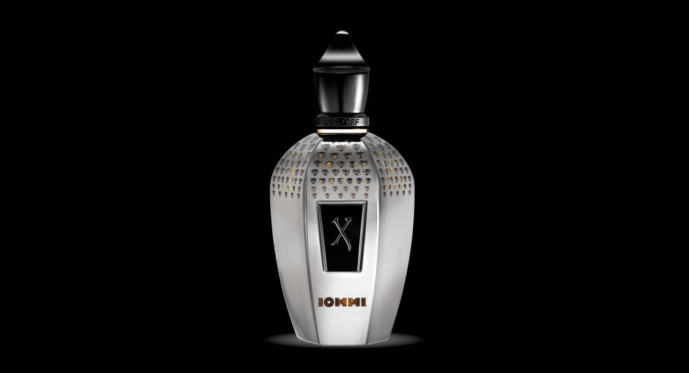 A metallic perfume bottle with a black cap stands against a black background. The bottle, inspired by Xerjoff's Iommi, features a studded design and a central black label adorned with crossed swords and the text "10MMI," creating an homage to Tony Iommi for multisensory experiences.