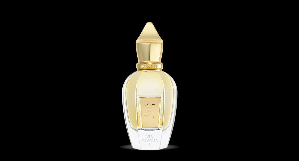 A transparent perfume bottle with a gold-toned cap and a gold label in the center, set against a black background. The label reads "Via Cavour 1," part of the Xerjoff Spotlight Collection.