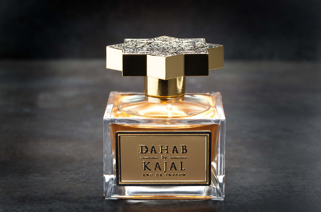 A clear glass perfume bottle with a gold and black star-shaped cap stands elegantly. The label reads "Dahab by Kajal - Classic Collection Eau de Parfum." This luxurious fragrance, in a 100ml EDP bottle, is placed on a dark, textured surface.