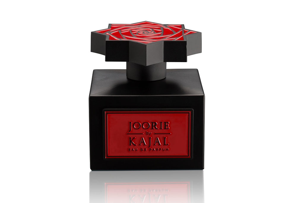 A black perfume bottle with a red label inscribed "Joorie from Kajal - Wardé Collection Eau De Parfum" evokes love and elegance. The star-shaped cap showcases an intricate red rose design.