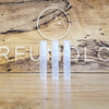 Three small, clear cylindrical containers are placed side by side on a wooden surface with the word "Perfumology" and a bird symbol engraved in the background, showcasing a Sample Subscription Pack that delivers curated perfume samples.