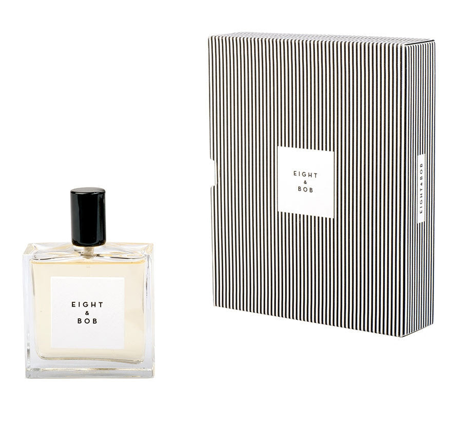 A bottle of Eight & Bob cologne stands next to its matching black-and-white striped box, both displaying the brand's label prominently.
