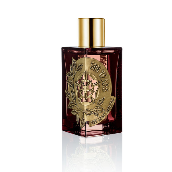 A glass perfume bottle with a golden cap and an ornate gold-embossed label reading "500 Years" exudes an air of enlightened beauty. The transparent amber liquid inside captures the essence of a Renaissance perfume, reminiscent of État Libre d'Orange's signature elegance.
