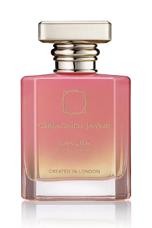 A rectangular bottle of Ormonde Jayne's Sakura Eau de Parfum, showcasing a gradient from pink to golden-yellow and infused with the essence of cherry blossom, is capped with a metallic lid. "Created in London" is elegantly etched at the bottom.