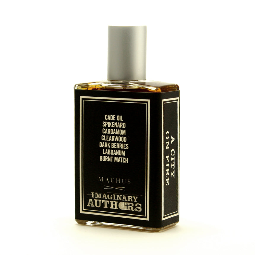 A bottle of perfume labeled "A City On Fire" by Imaginary Authors features a refined smoke accord with ingredients like cade oil, spikenard, cardamom, clearwood, dark berries, labdanum, and burnt match.