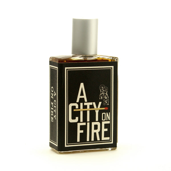 A rectangular perfume bottle with a label that reads "A City On Fire" by Imaginary Authors. The bottle has a silver cap and black and white packaging, encapsulating an inviting scent with a refined smoke accord.