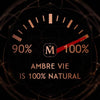 A gauge pointing to 100% with text below stating "House of Matriarch Ambre Vie is 100% Natural," highlighting its ultra-natural amber essence, and a logo featuring the letter "M" in the center.