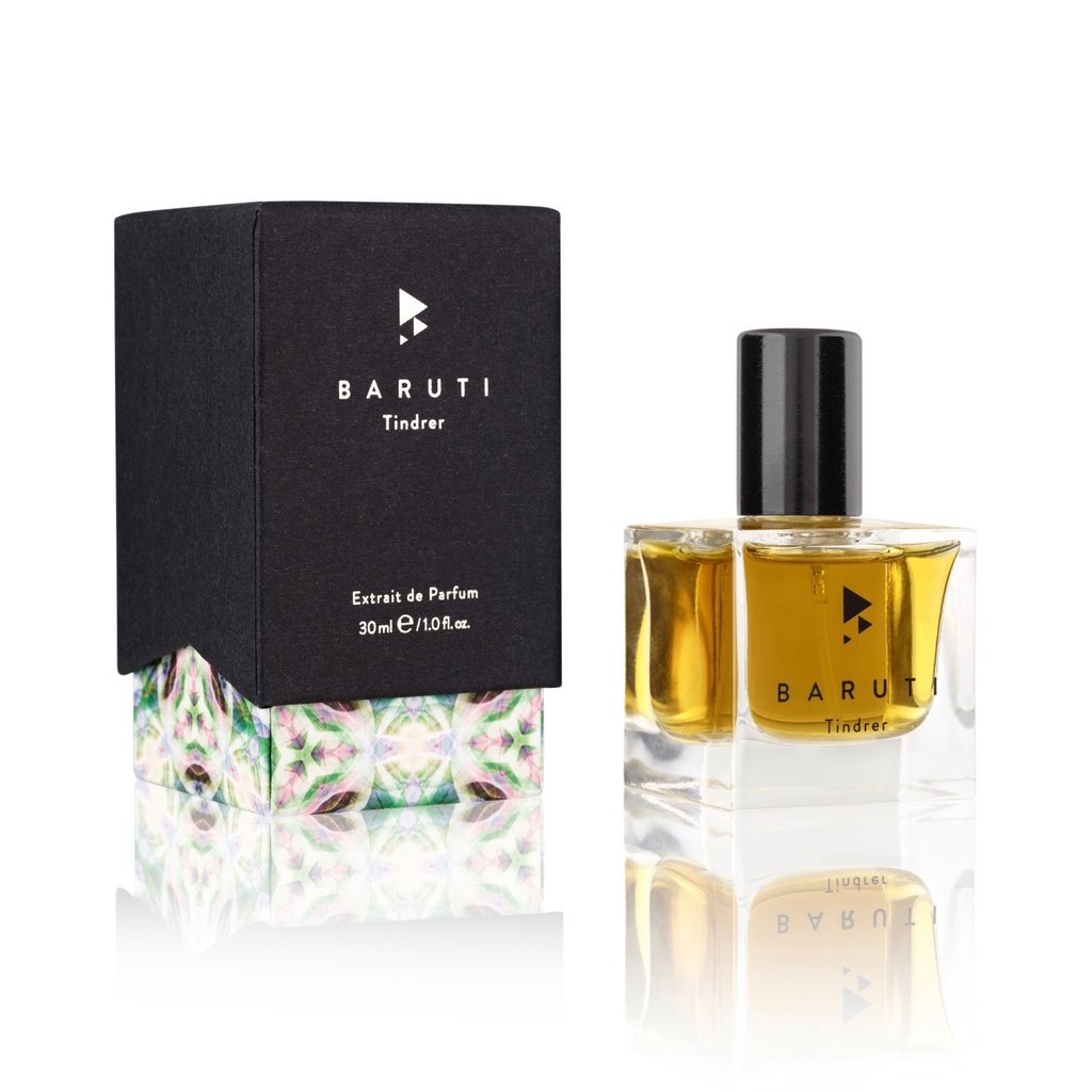 A 30ml bottle of Baruti's Tindrer Extrait de Parfum, exuding a nostalgic vibe, is displayed next to its black box packaging which rests on a floral-patterned base.