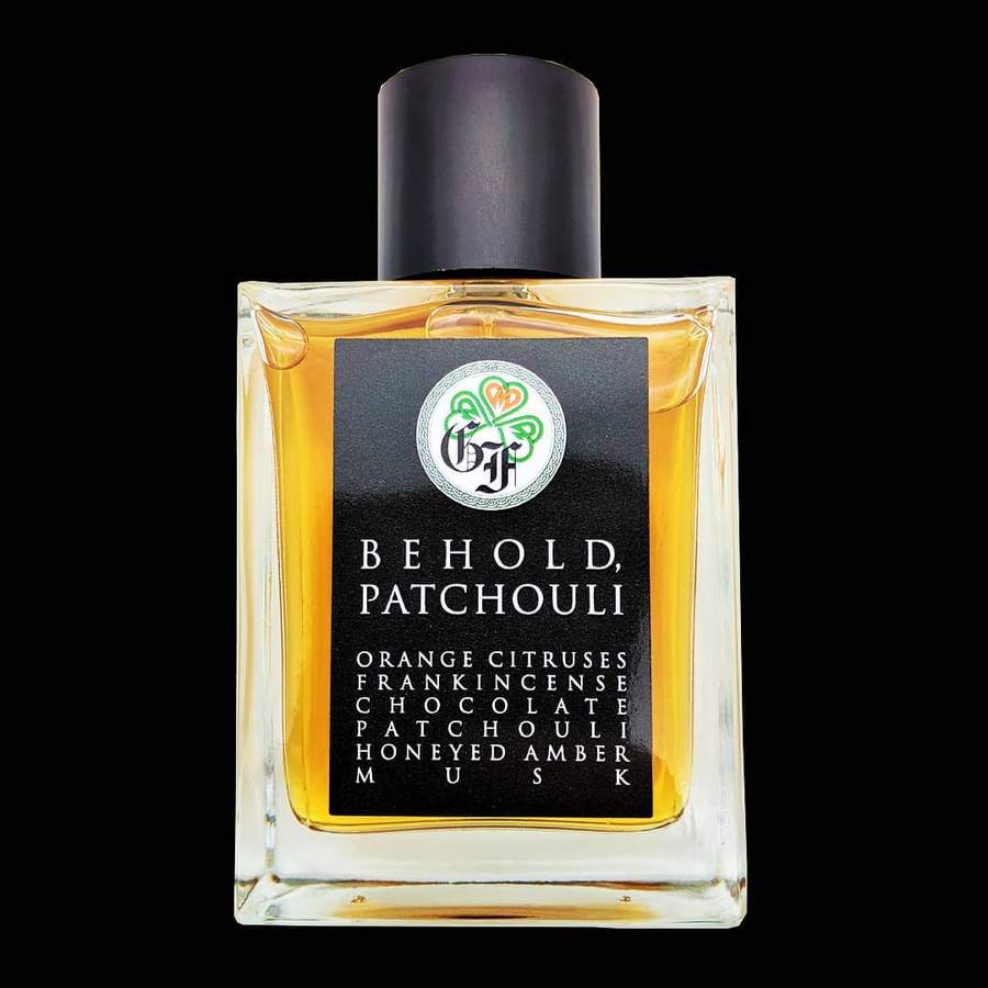 A square perfume bottle with a black cap labeled "Behold Patchouli" by Gallagher Fragrances. The label lists notes of orange citruses, frankincense, chocolate, patchouli, honeyed amber, and musk.