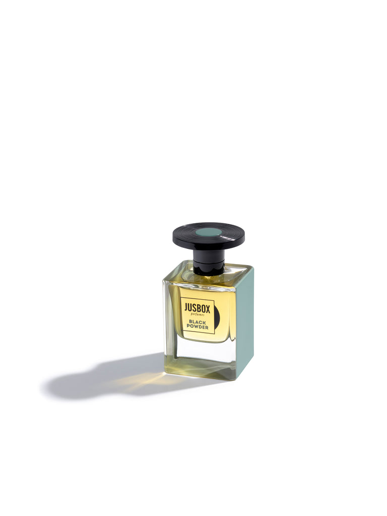 A bottle of Jusbox Black Powder, reminiscent of the rebellious spirit of Generation X, contains yellow liquid. It features a rectangular glass body and a black round cap, set against a white background.