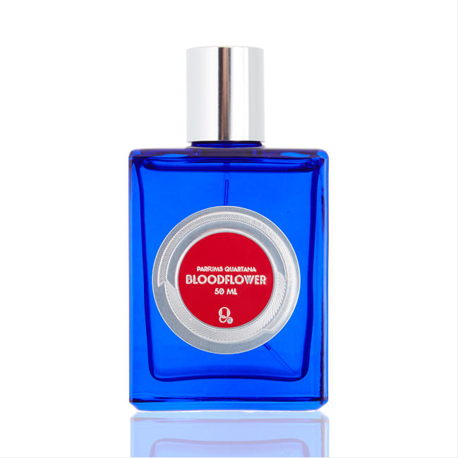 A blue perfume bottle with a silver cap, featuring a silver and red circular label that reads "Bloodflower by Parfums Quartana" and "50 ML," evoking the mysterious allure of dark rose.
