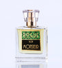 A glass bottle of "Bon Monsieur" by Rogue Perfumery with a gold cap and a green and black label sits on a white surface, exuding the classic charm of a gentlemen's fragrance with hints of fougeres and lavender.