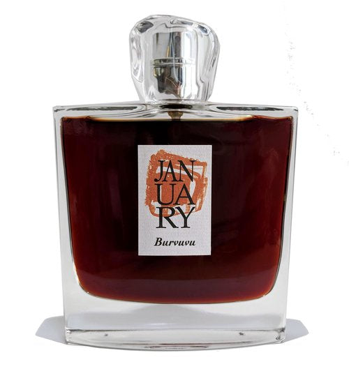 A rectangular glass perfume bottle labeled "January Scent Project Burvuvu" with dark amber liquid inside and a silver cap, exuding hints of cedar and amber.