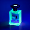 A square glass bottle of Jusbox's "Cheeky Smile" perfume is bathed in a blue glow, evoking the energetic essence of Acid House, set against a dark backdrop.