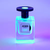 A bottle of Jusbox's "Cheeky Smile" fragrance, its fluorescent packaging illuminated with blue and purple lighting against a gradient background.