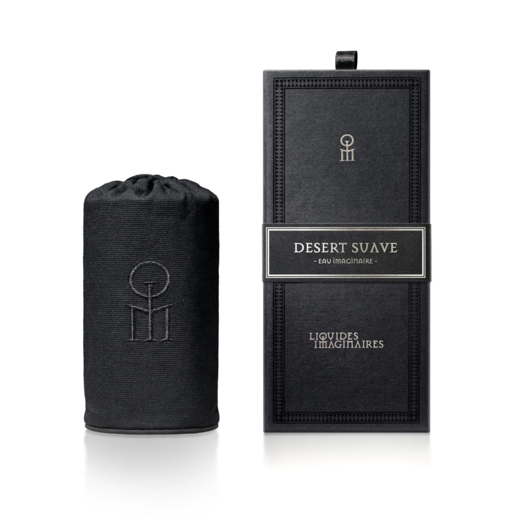 A black cylindrical bottle in a fabric pouch sits next to a black rectangular box labeled "Desert Suave" by Liquides Imaginaires, subtly hinting at the aromatic notes of cardamom.