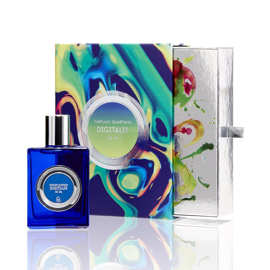 A blue bottle of "Digitalis" perfume from Parfums Quartana sits beside a colorful, patterned box with a metallic exterior. This ozonic fragrance captures the essence of the mysterious foxglove flower, blending nature's elegance with modern sophistication.