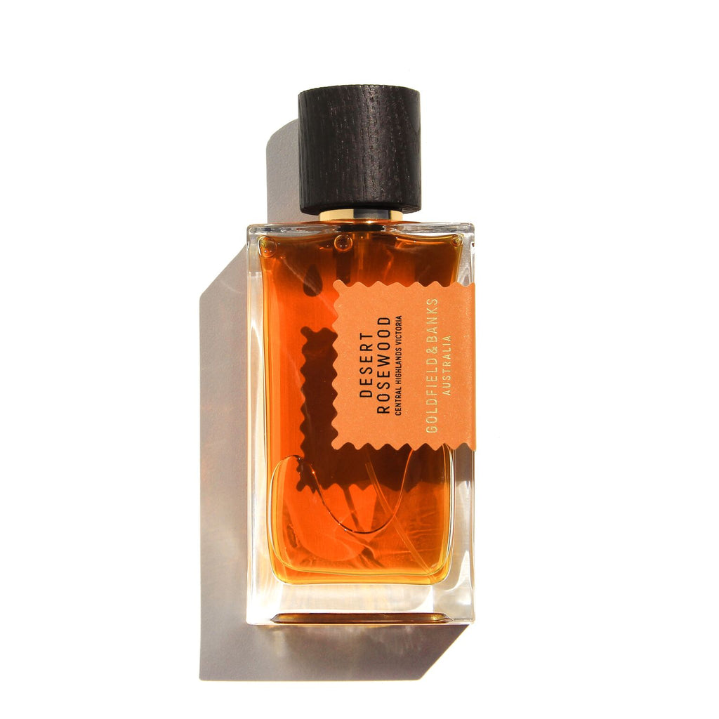 A clear glass fragrance bottle labeled "Desert Rosewood" by Goldfield & Banks, featuring an amber-colored liquid and a black cap. This leathery scent encompasses notes of wood and spice, capturing the rugged elegance of desert landscapes.