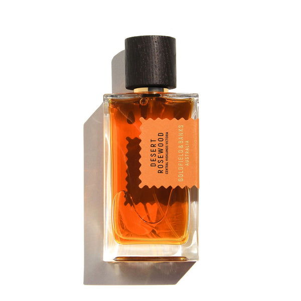 A clear glass fragrance bottle labeled "Desert Rosewood" by Goldfield & Banks, featuring an amber-colored liquid and a black cap. This leathery scent encompasses notes of wood and spice, capturing the rugged elegance of desert landscapes.