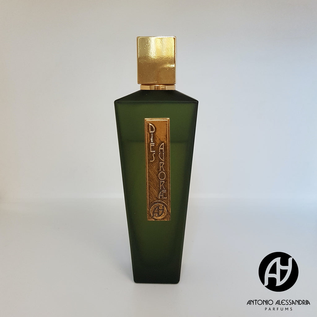 A dark green perfume bottle with a gold cap and label, showcasing the name "Dies Aurorae." The brand "Antonio Alessandria" along with its logo is visible in the lower right corner. This fragrance encapsulates the essence of a Sicilian religious feast, with woody notes that evoke a sense of tradition and reverence.