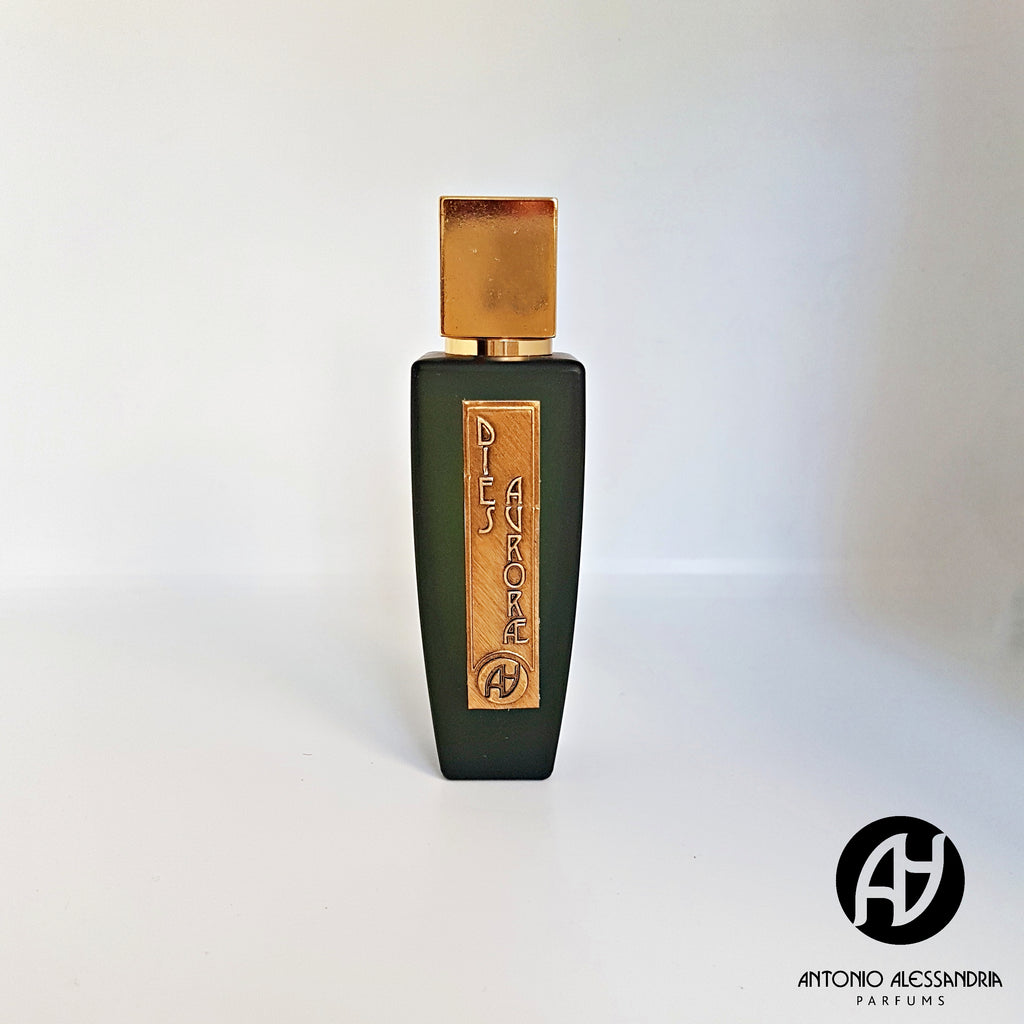 A black perfume bottle with a gold label and cap is centered. The label reads "Dies Aurorae." Reminiscent of the grandeur of the Saint Agata feast, its woody facets evoke deep tradition. The Antonio Alessandria logo graces the bottom right corner.