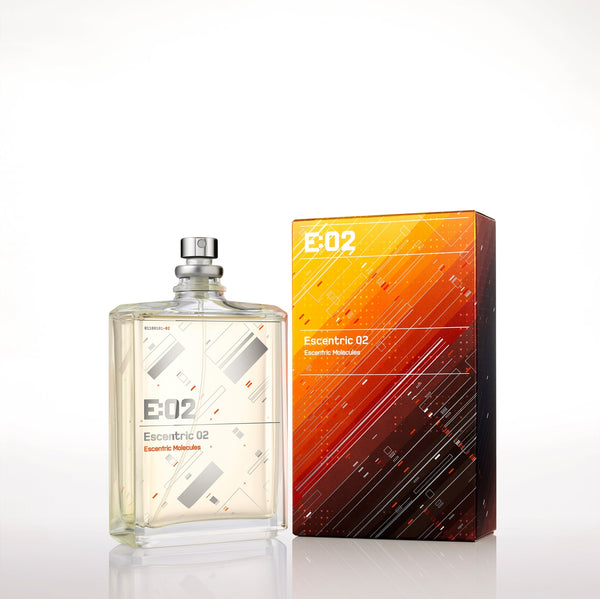 A bottle of Escentric 02 by Escentric Molecules stands next to its rectangular packaging. The bottle is clear with a minimalist design, and the box features an abstract, geometric pattern in warm colors. This fragrance exudes super-longlasting freshness, enriched with the elegance of Ambroxan and hedione.