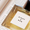 A bottle of Eight & Bob's Eight & Bob exclusive cologne rests on an open book, partially covering the text on the pages.