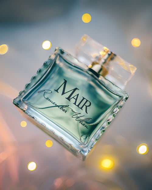 A glass perfume bottle labeled "Mair Remember When" is showcased against a backdrop of blurred yellow lights, capturing the essence of jasmine complemented by subtle hints of Italian bergamot.