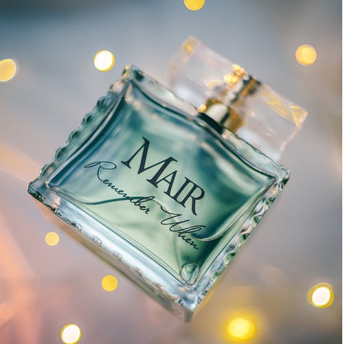A glass perfume bottle labeled "Mair Remember When" is showcased against a backdrop of blurred yellow lights, capturing the essence of jasmine complemented by subtle hints of Italian bergamot.