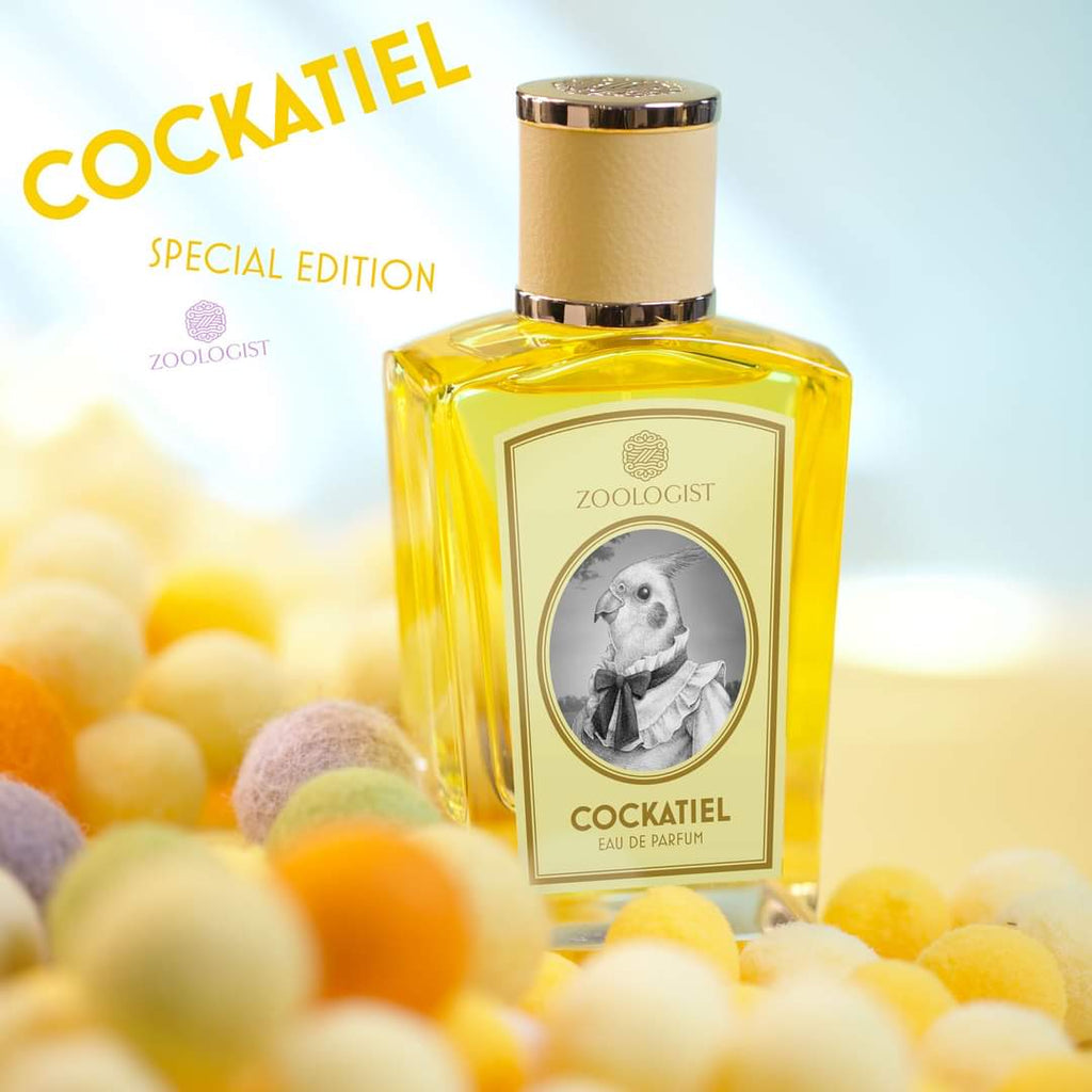 A bottle of "Cockatiel" by Zoologist perfume is displayed among pastel-colored balls, evoking the vibrant essence of an Australian spring. The label features an illustration of a cockatiel bird in a suit, complemented by hints of yellow acacia.