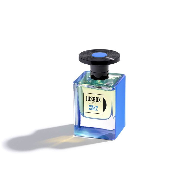 A Jusbox perfume bottle labeled "Feel 'n' Chill" with a blue-tinted exterior and black cap offers an aromatherapeutic fragrance designed for relaxation, crafted by the renowned Dominique Ropion.