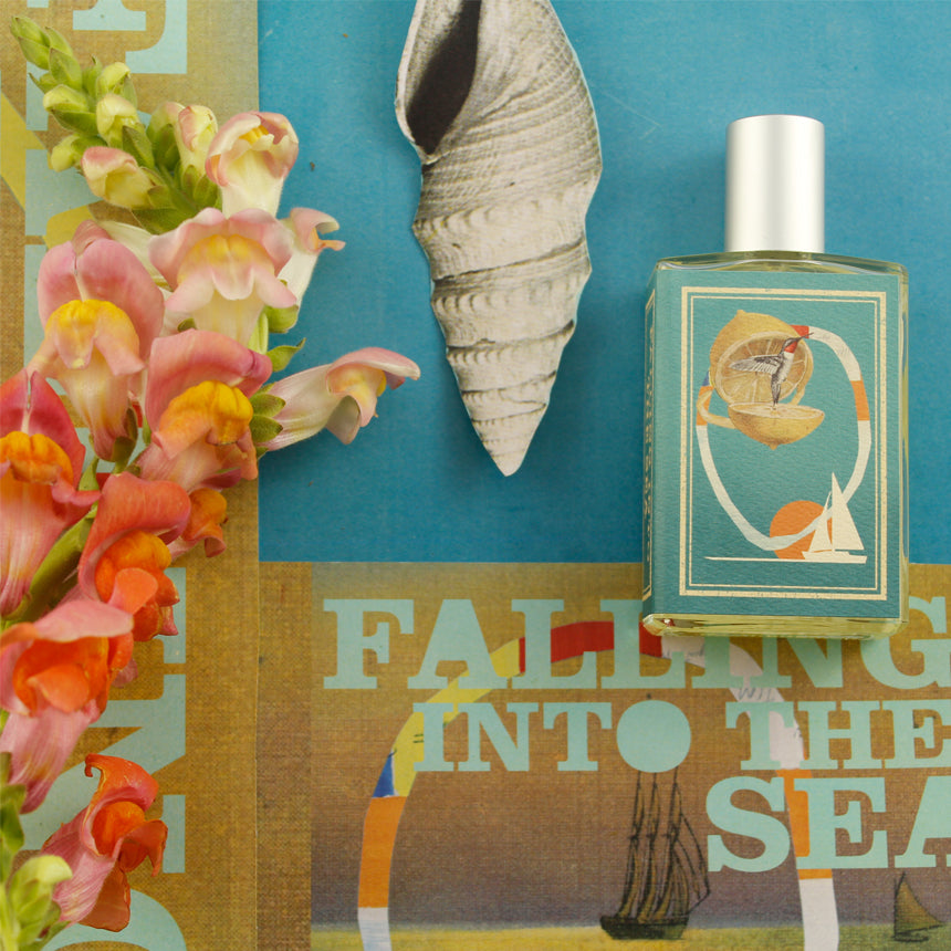 A bottle of fragrance with ocean-themed packaging is placed next to pink and orange flowers on a colorful backdrop, capturing the essence of a refreshing summer scent, with the words "Falling Into the Sea" by Imaginary Authors.