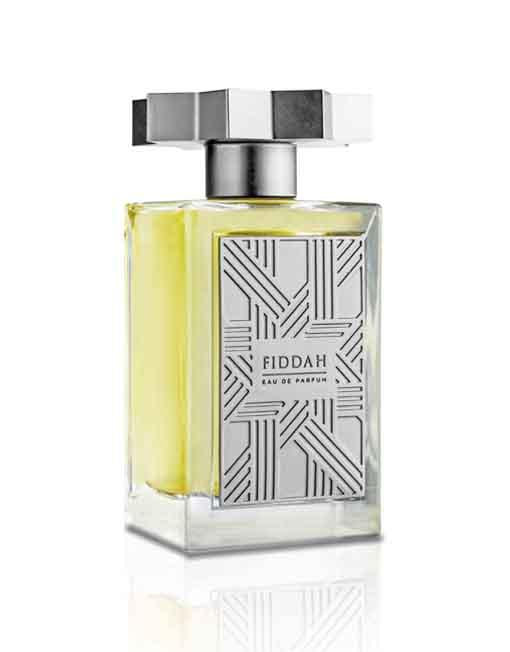 A rectangular glass bottle of Fiddah Eau de Parfum from the Kajal - Fiddah Collection, featuring a geometric silver label and matching silver cap, contains a yellowish liquid that exudes smoky leather scents, making it perfect for those seeking a sensual romantic fragrance.