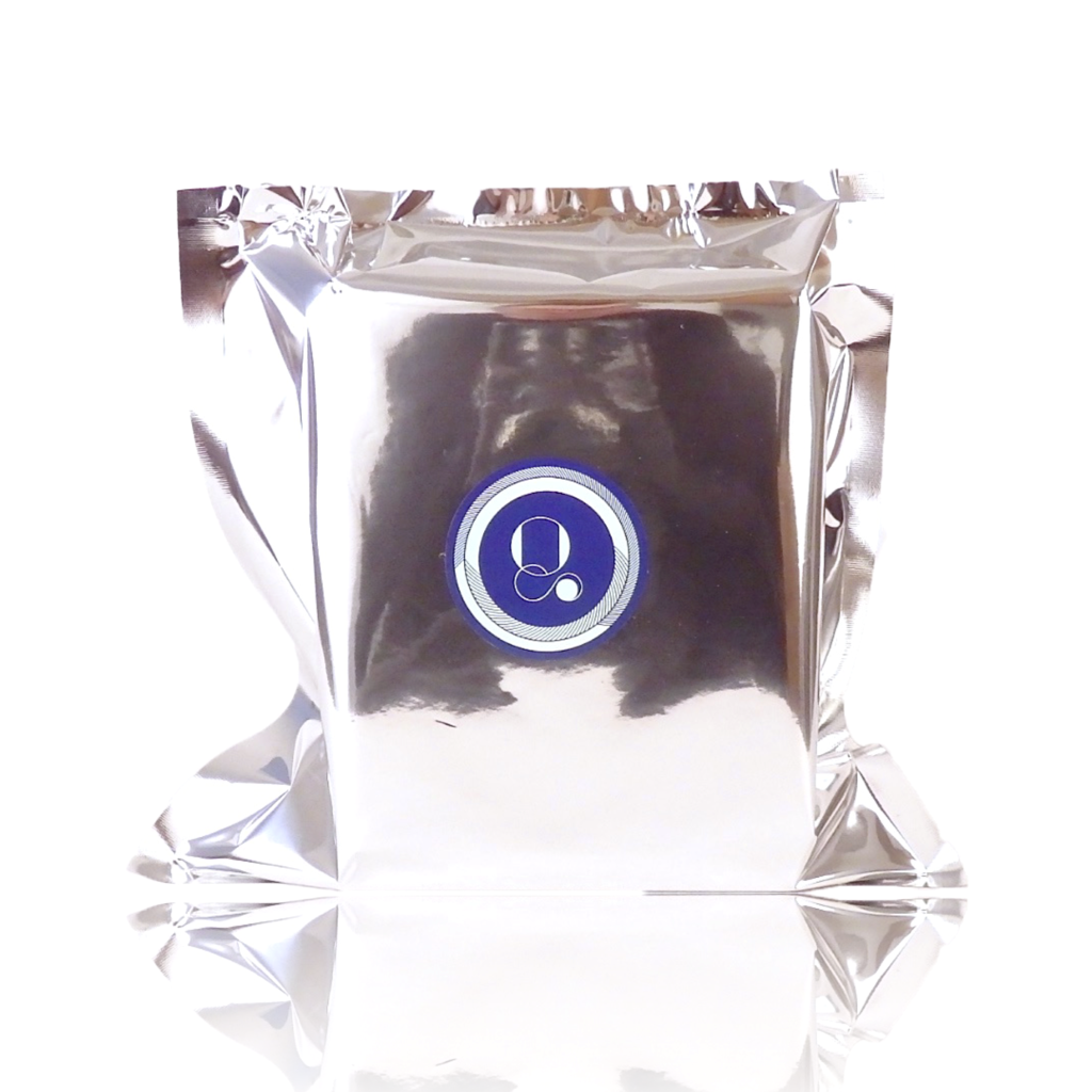 A silver foil package with a blue circular logo featuring a white lowercase "q" and a dot in the center, emanating an ozonic fragrance of Digitalis by Parfums Quartana.