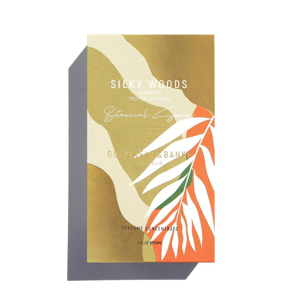 A rectangular perfume box adorned with abstract leaf designs and text that reads: "Silky Woods, Goldfield & Banks, Australia, Botanical Série, Perfume Concentrate, Agarwood from Tropical Australia, 3.4 FL.OZ / 100mL." Experience the allure of this luxury fragrance encapsulated in elegant packaging.