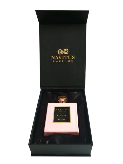 A bottle of Eidola by Navitus Parfums in a pink container is placed inside an open black box with gold text on the lid, exuding the elegance of French Rose crafted by master perfumers.