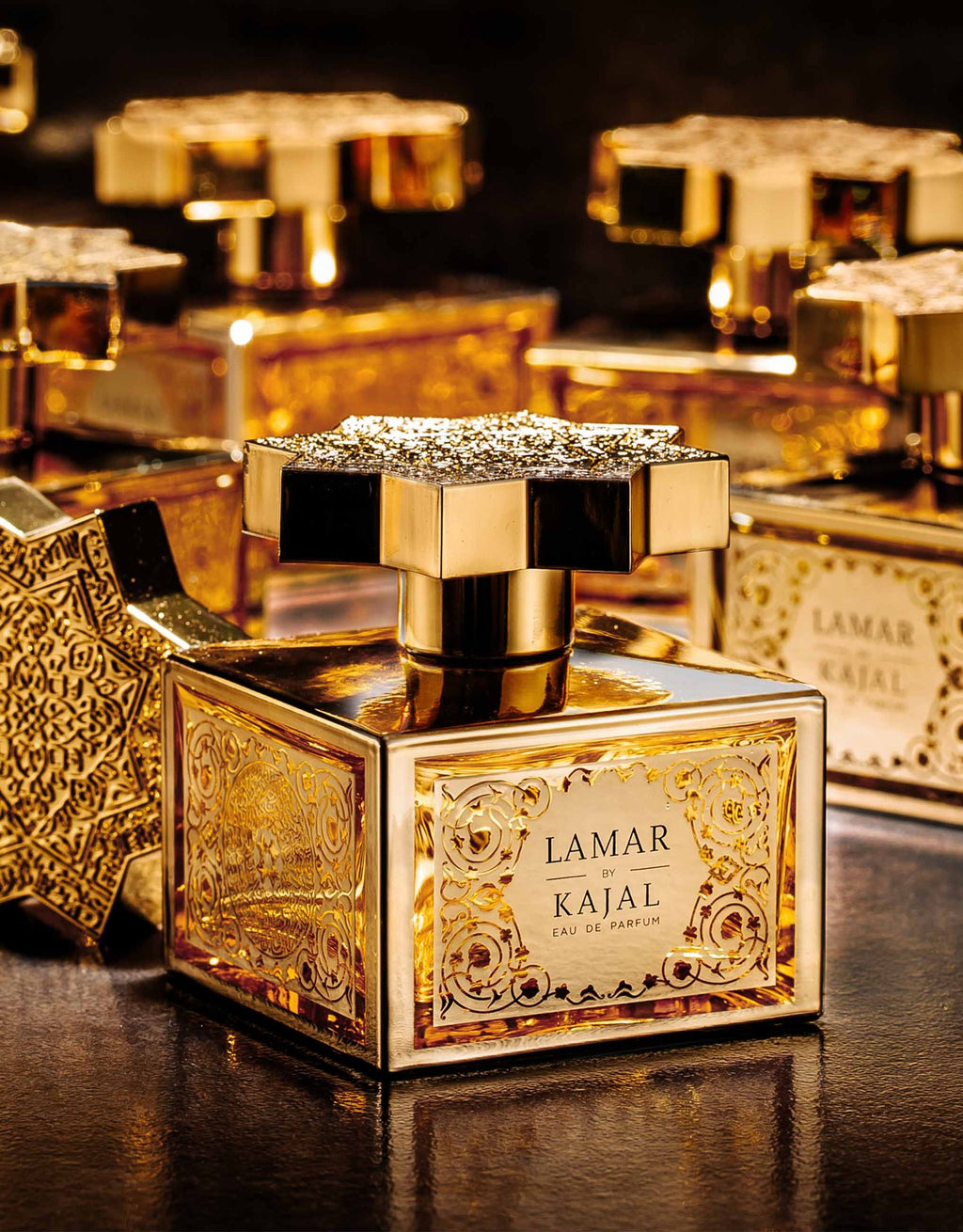 Perfume bottles adorned with gold caps and intricate designs, featuring the label "Lamar by Kajal - Classic Collection Eau de Parfum" on a reflective surface, evoke a sense of Mediterranean breeze with each spritz.