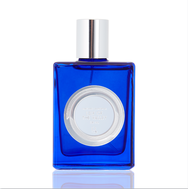A rectangular blue glass perfume bottle with a silver cap and a circular silver label on the front displaying "Lily of the Valley" by Parfums Quartana features an enticing Eau de Parfum blend.