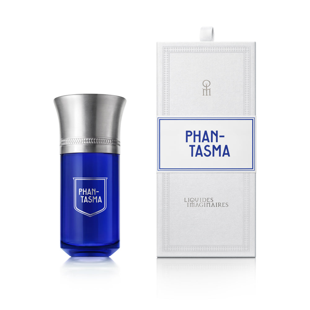 A blue perfume bottle with a silver cap labeled "Phan-Tasma" sits next to its white box, which features both "Phan-Tasma" and "Liquides Imaginaires" branding. The scent hints at sensual wood and black tea, evoking an air of mystery.
