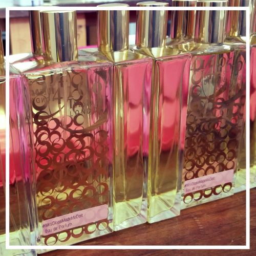 Four rectangular perfume bottles with golden caps are lined up. The bottles have decorative golden patterns and the label reads "#MrsGlossMadeMeDoIt Eau de Parfum" by 4160Tuesdays, adding an air of mystery to the otherwise sophisticated array.