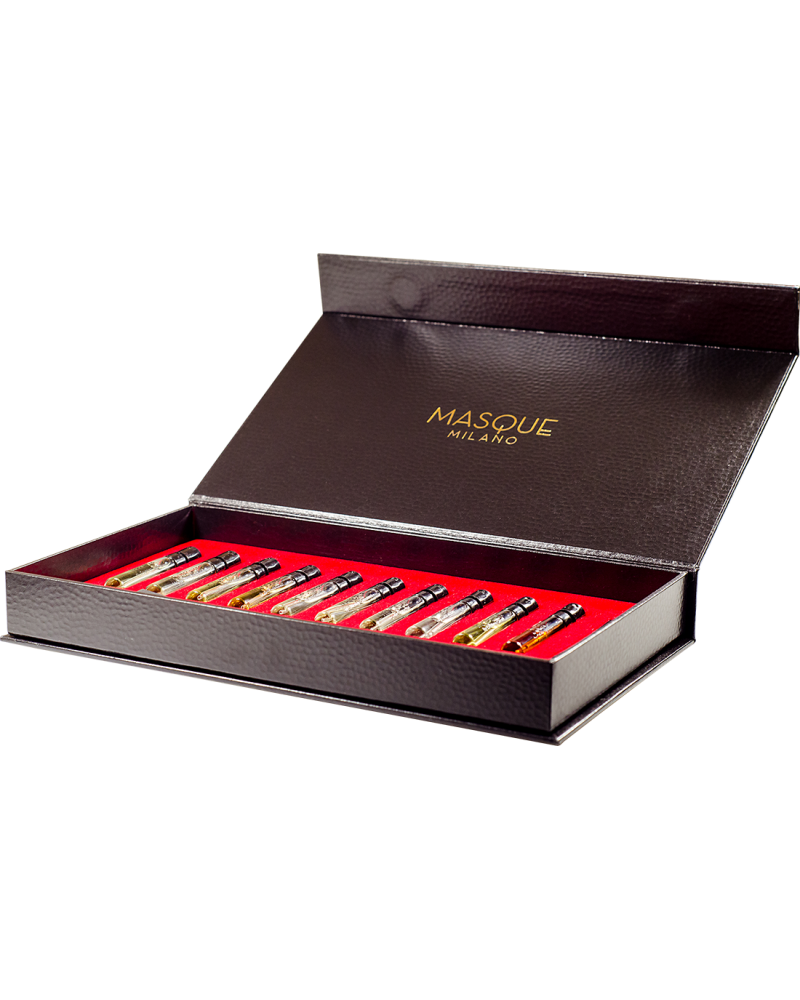 A black box with a red interior from the Masque Milano Opera Collection Discovery Kit contains sixteen 2ml small glass vials labeled with various perfumes, including the evocative "Montecristo," and has "MASQUE MILANO" written on the inside of the lid.