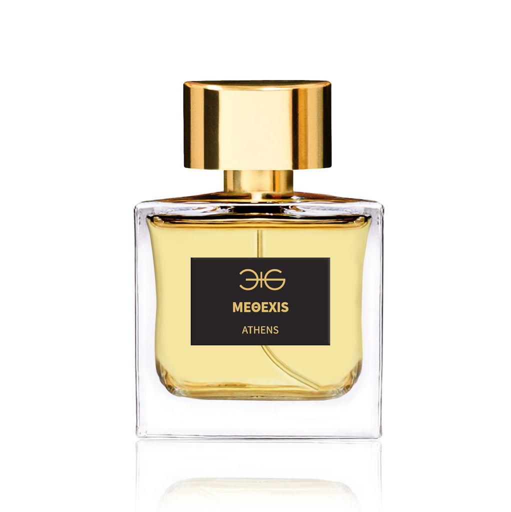 A square glass bottle of perfume filled with yellow liquid, featuring a black label reading "Manos Gerakinis METHEXIS" and a gold cap. The METHEXIS fragrance boasts a fig scent and is crafted using plant-based alcohol.