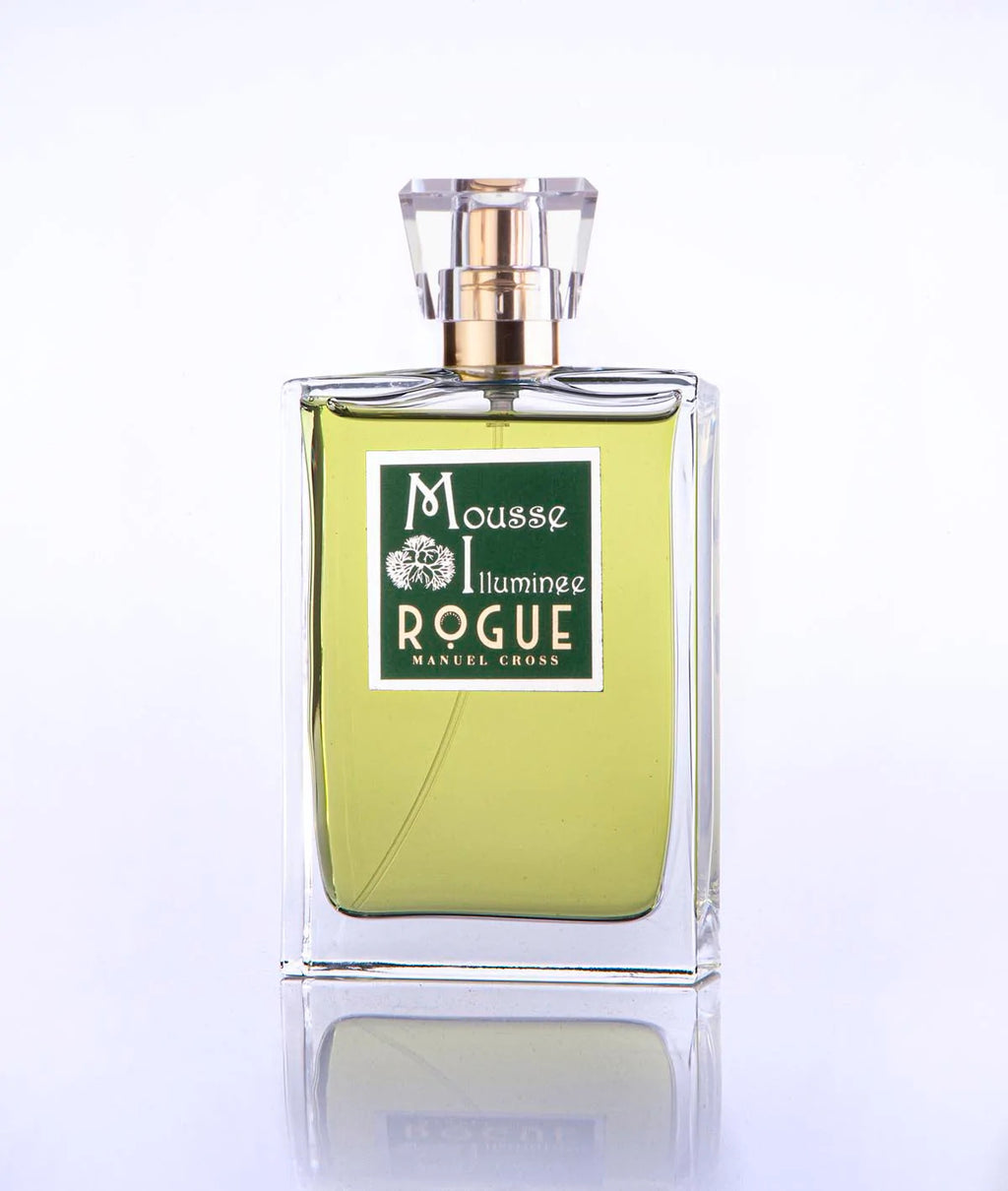 A clear rectangular perfume bottle with green liquid and a sophisticated label reading "Mousse Illuminee Rogue Perfumery," topped with a geometric design cap, exudes notes of Green Cypress.