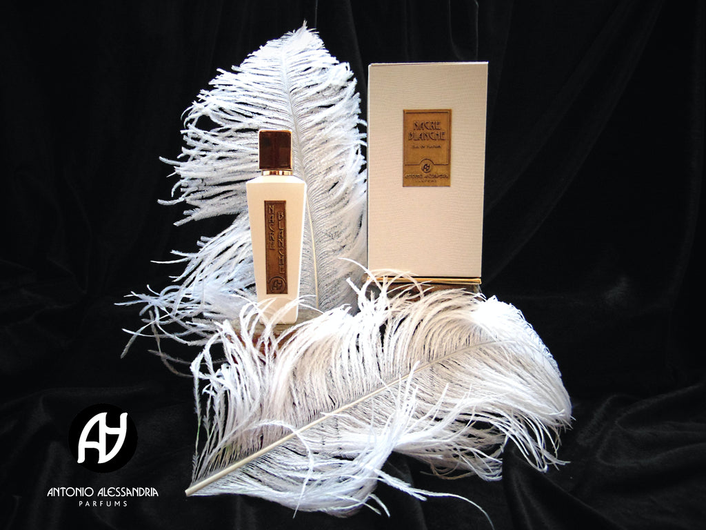 A white perfume bottle and its matching box labeled "Nacre Blanche" are placed on white feathers, exuding an enticing floral fragrance. The Antonio Alessandria logo is visible in the corner on a black background.