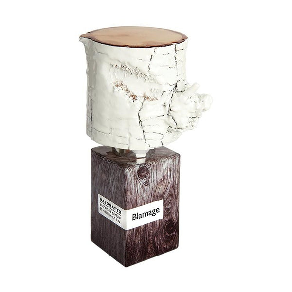 A bottle of Blamage by Nasomatto features a wooden texture and a white, textured cap that resembles a tree trunk.